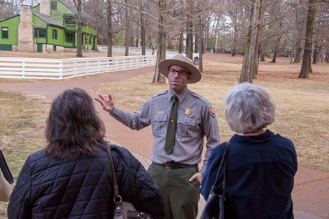 Park Ranger standing in front of a group of people with a green house in the background.