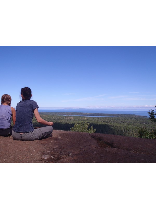 Two people sit on a rocky outcropping over looking a forest and lakes on an island in Lake Superior.
