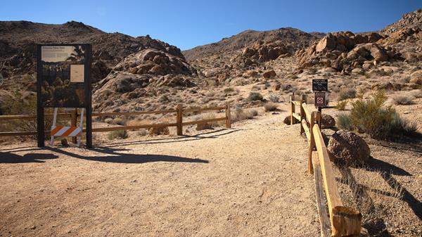 A dirt trail between two split rail fences heading towards a ridge in the distance.
