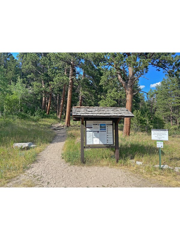 View of the Sandbeach Lake Trailhead. The trail is located to the left of the bulletin board.