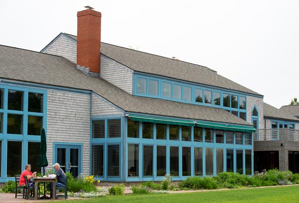 A two story grey building lined with windows and blue trim in front of a green lawn