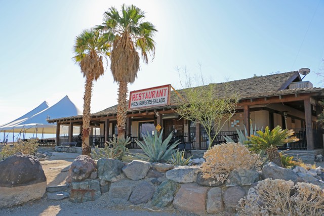 A one-story restaurant building with desert plants landscaped around it and two palm trees