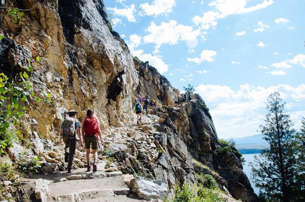 Hikers walk up a rocky trail with a cliff on the right.