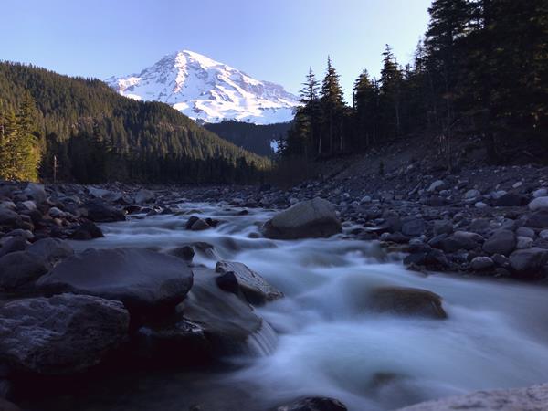 A river flows through a rocky riverbed in a valley on the slopes of a glaciated mountain.