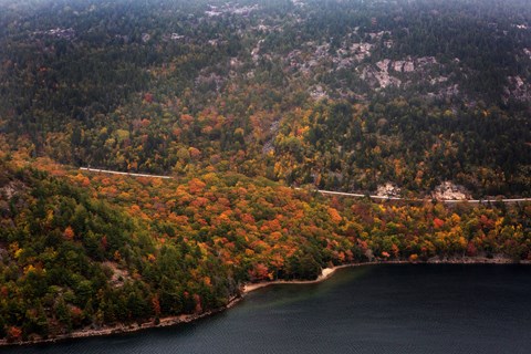 A road goes through brightly colored leaves around a mountain above a lake.