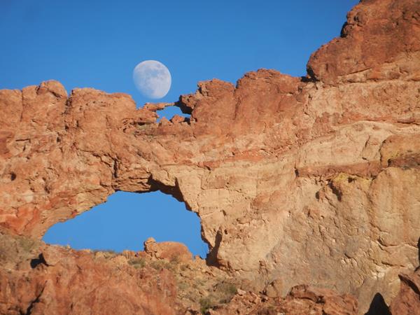 The moon rises behind two natural rock arches, stacked upon one another.