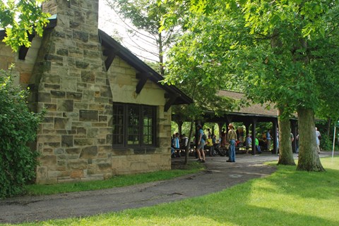A crowd gathered around picnic tables under a rustic shelter made of sandstone and dark brown wood.