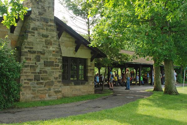 A crowd gathered around picnic tables under a rustic shelter made of sandstone and dark brown wood.