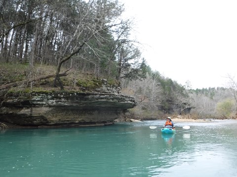 A paddler in a blue kayak floats past an undercut rock feature on the Buffalo River.