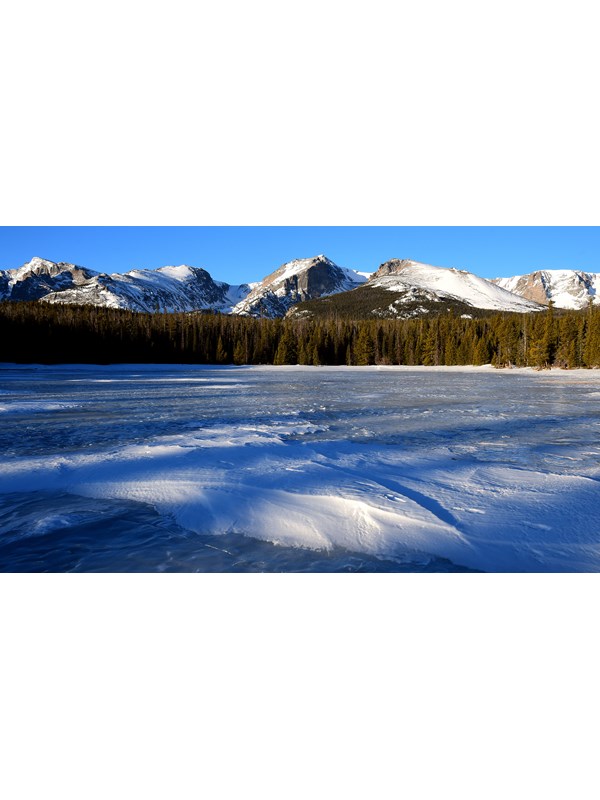 The lake is frozen with a layer of snow on top. Mountains in the distance are covered with snow