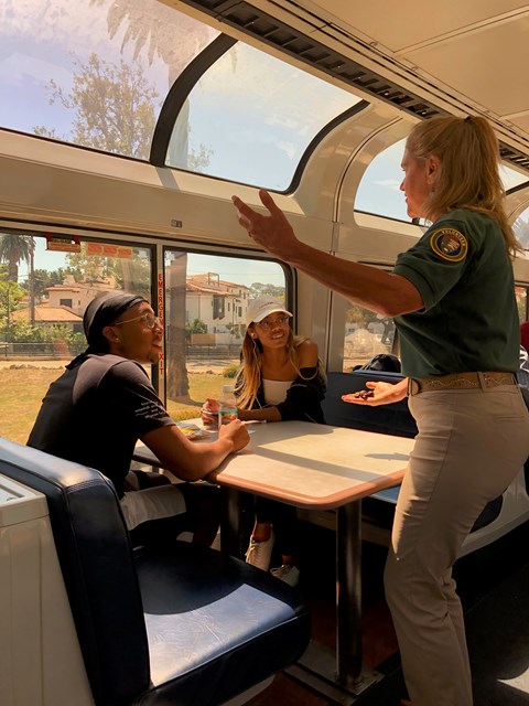 A volunteer is talking to two railroad passengers onboard a train.
