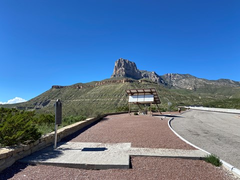 A roadside picnic shelter stands below a prominent mountain peak.