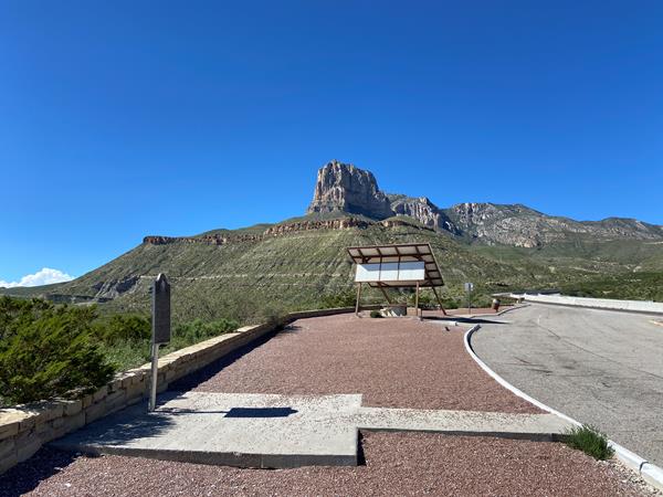 A roadside picnic shelter stands below a prominent mountain peak.