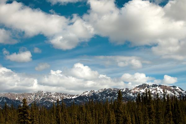 puffy white clouds in a blue sky over a ridge dappled with snow