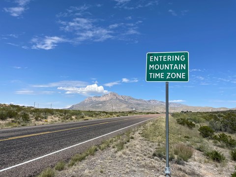 A sign reads "Entering Mountain Time Zone" with Guadalupe Mountains in the Background