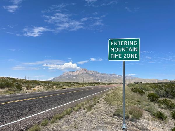 A sign reads "Entering Mountain Time Zone" with Guadalupe Mountains in the Background