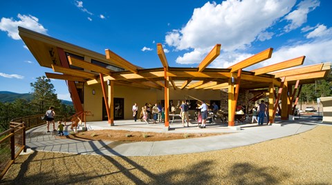 People mill around a modern building with wood beams radiating out from the roof.
