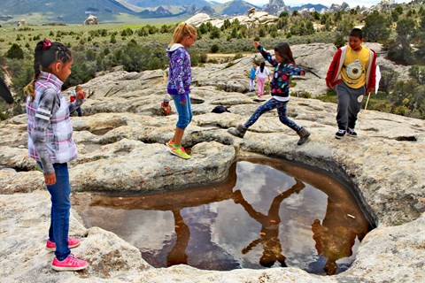 Kids play around a water filled depression on a granite slab formation.
