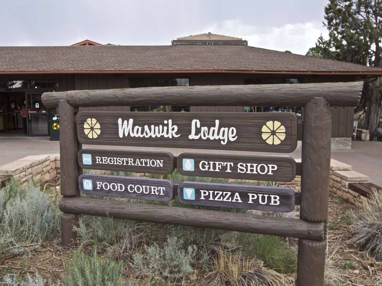 Wooden sign in front of single story lodge building reads Maswik Lodge, Registration, Gift Shop etc.