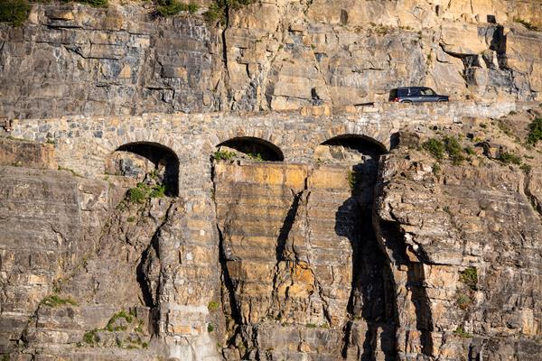 Car drives uphill over triple arched stone bridge
