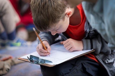 A kid works on a paper attached to a clipboard.