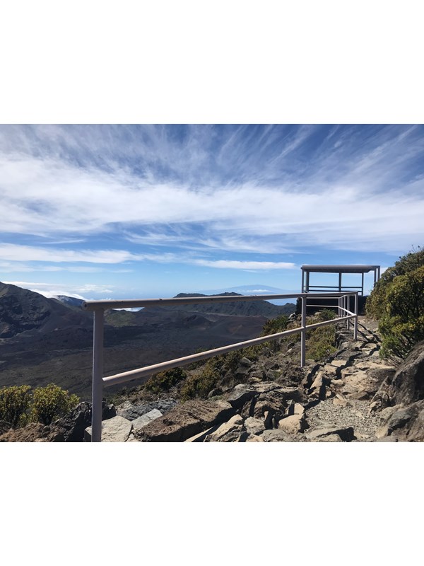 A path with a railing leads to an overlook next to a deep volcanic valley