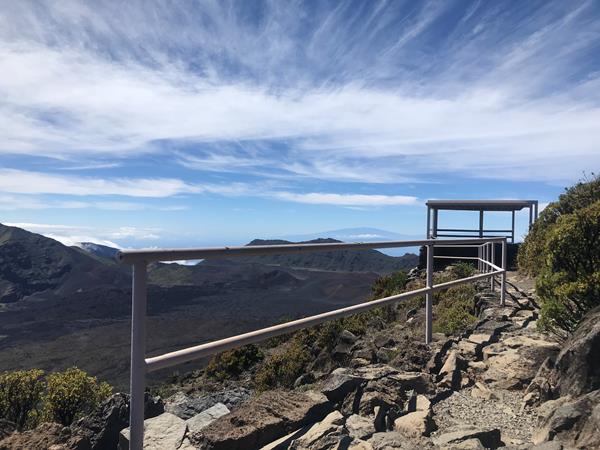 A path with a railing leads to an overlook next to a deep volcanic valley