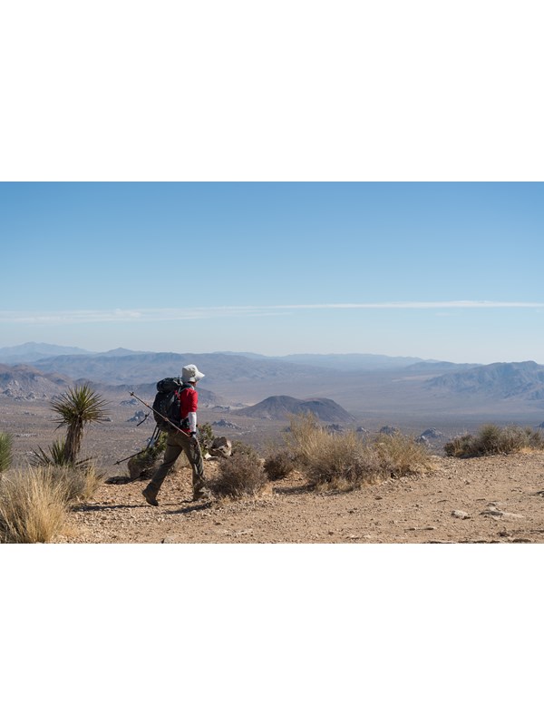 A person hiking a dirt trail on a mountain with mountains in the distance.