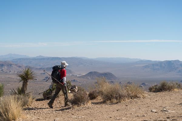 A person hiking a dirt trail on a mountain with mountains in the distance.