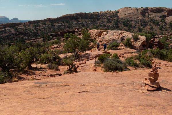 Stacked rocks guide two hikers across sandstone and juniper trees