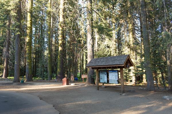 A wooden kiosk, with maps on it stands behind the road and shuttle parking spot.