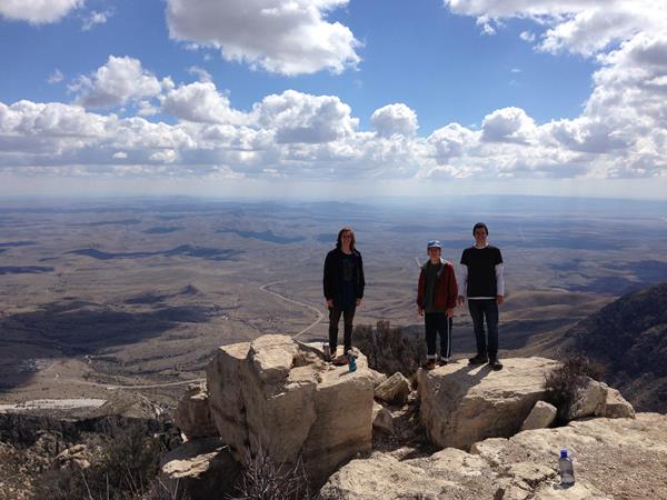 Three people stand on the summit of a mountain peak
