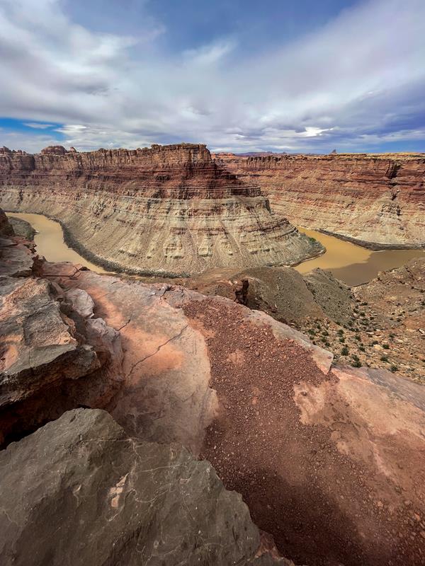 A green and gray river converge below towering canyon walls