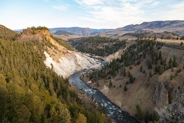 A river runs through a canyon. Steam is released from a thermal area near a bend in the river.