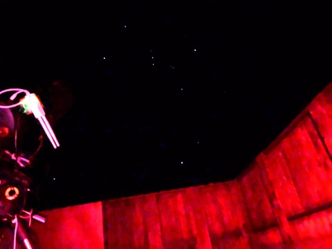 A telescope points at the sky in a wooden structure.