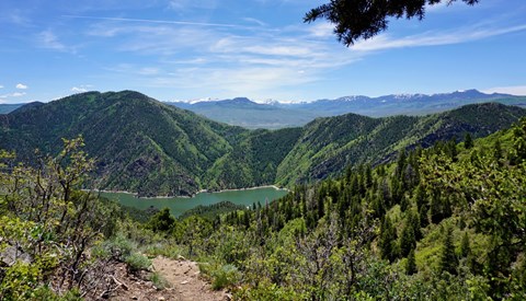 A trail with a view of mountains and overlooking a dam in the distance
