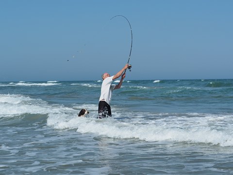 A person stands in the water and casts a fishing pole.