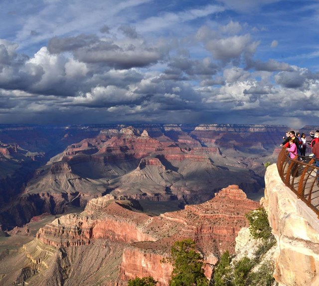 People behind guardrails at a scenic overlook viewing a colorful landscape of peaks and cliffs.