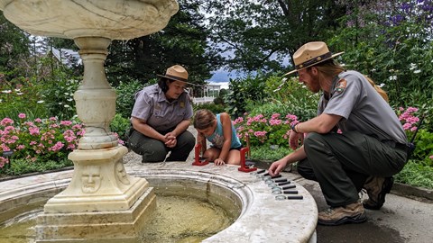 Two park rangers kneel with a child while she looks in a microscope