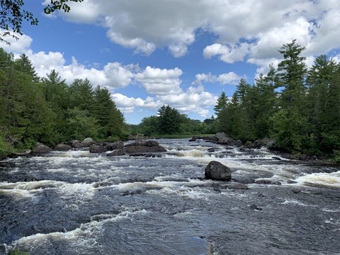 A landscape image of a large river flowing down and over large volcanic rocks that form rapids.