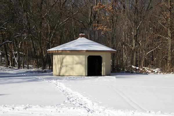 Snow covers the ground. A white and brown hut with a large opening provides warmth for skiers.