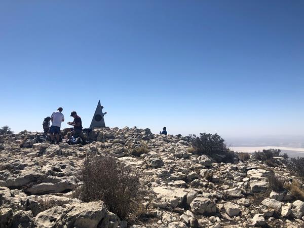 groups of people sit and stand on a stony summit.