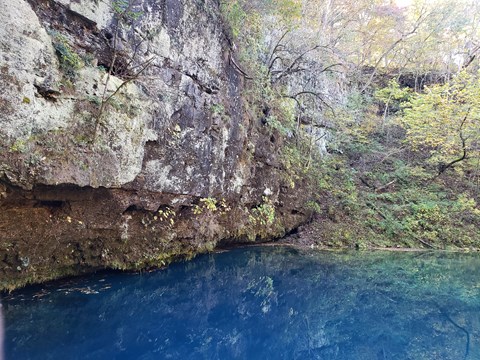 a deep dark blue spring at the bottom of a cliff of gray rock