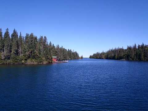 A red historic summer cottage mail room and dock can be seen along the conifer lined Tobin Harbor.