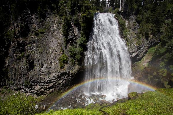 A waterfall cascades off a cliff with a rainbow arching through the mist of the waterfall.