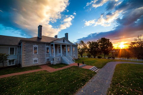 The rising sun lights the clouds over an antebellum stone mansion with a white portico.
