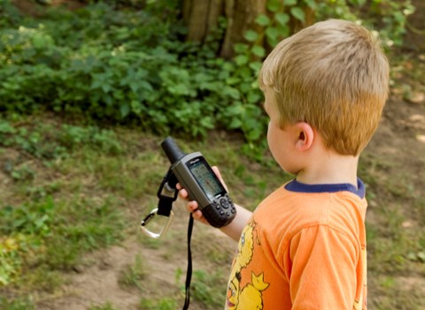 A boy wearing an orange shirt holds a GPS device in his hand
