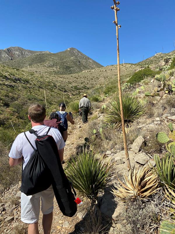 A uniformed park ranger and visitors hike up a desert trail