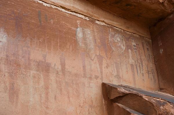 Faint red, white, & brown painted markings of tapered human figures on a sandstone wall