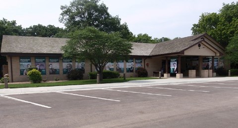 An l-shaped brick building with landscaped bushes and trees surrounding it.